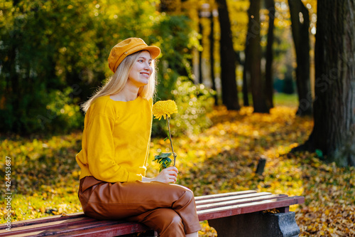 Style blond girl in yellow pullower sitting at bench in autumn park. Pretty woman outside. photo