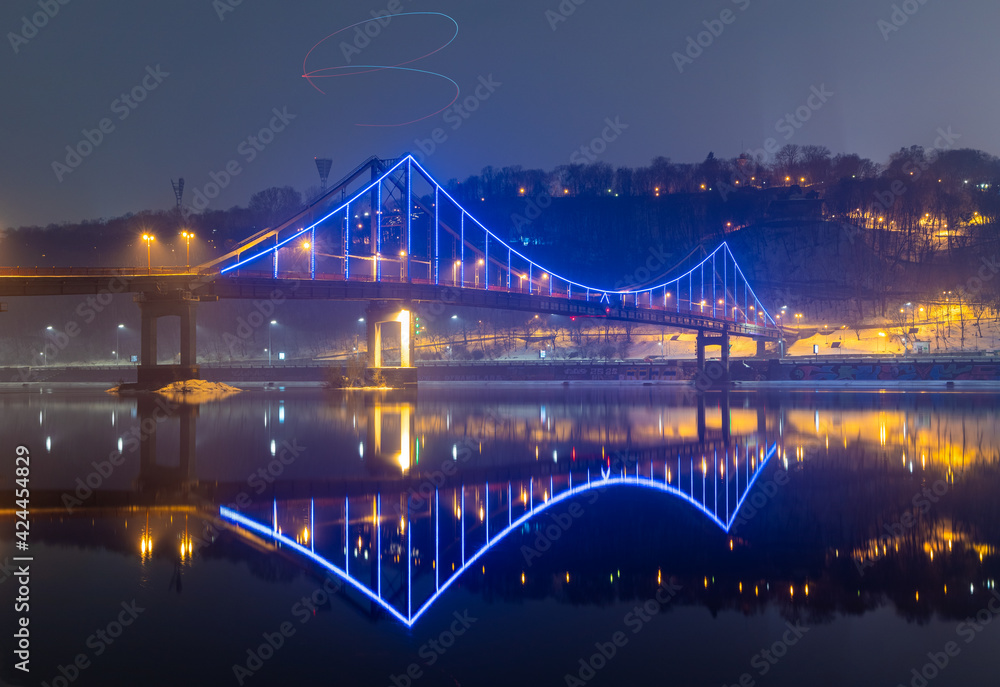 Obraz premium Pedestrian bridge in Kiev. Evening lighting. Reflection of the bridge in the river.