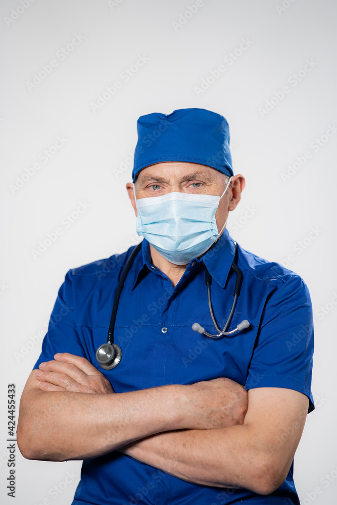 Portrait of happy senior doctor with folded arms and mask on face isolated on white background. Confident male doctor in a blue labcoat and stethoscope looking at camera. Portrait of handsome mature Portrait of happy senior doctor with folded arms and mask on face isolated on white background. Confident male doctor in a blue labcoat and stethoscope looking at camera. Portrait of handsome mature