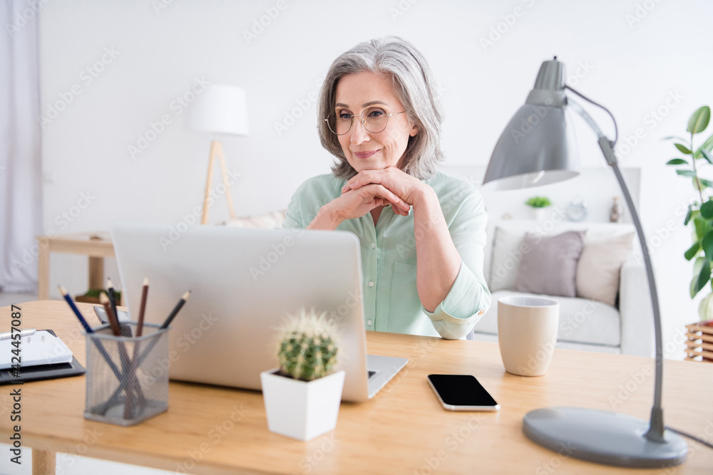 Portrait of minded focused woman sitting behind desktop arms under chin look interested laptop indoors Portrait of minded focused woman sitting behind desktop arms under chin look interested laptop indoors