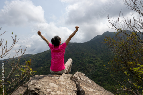 Cheering young woman open arms on mountain top