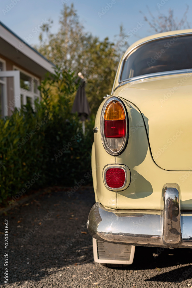 Close up of taillight of a vintage car parked in a sunny front yard.