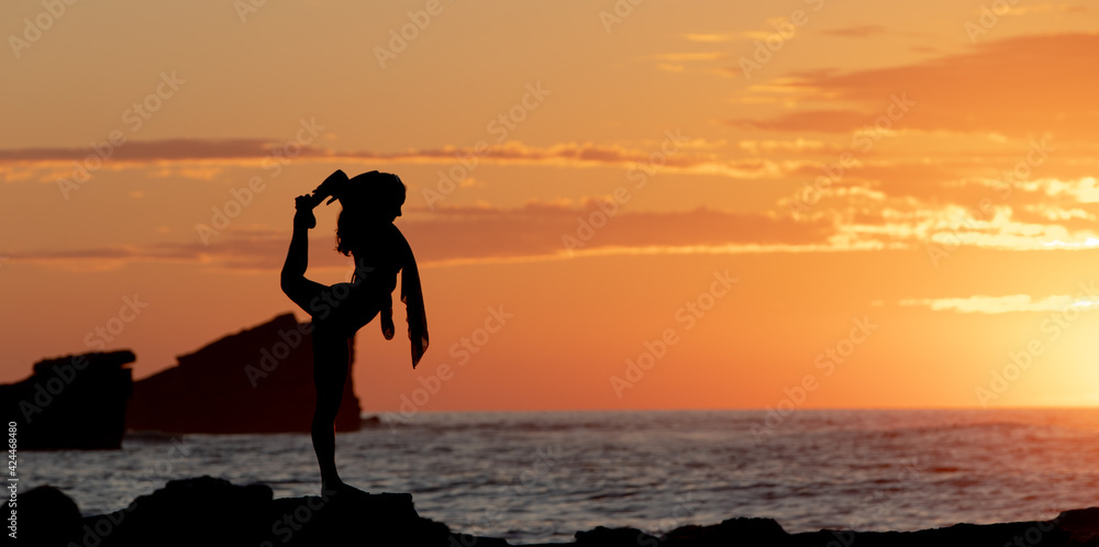 silhouette of woman doing yoga dancer pose on beach at sunset