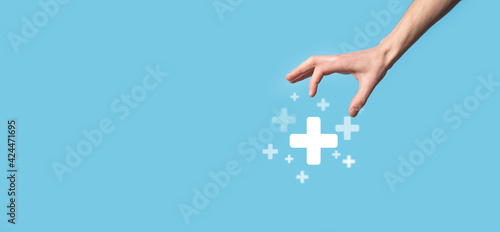 Fototapeta Naklejka Na Ścianę i Meble -  Male hand holding plus icon on blue background. Plus sign virtual means to offer positive thing like benefits, personal development, social network Profit,health insurance, growth concepts