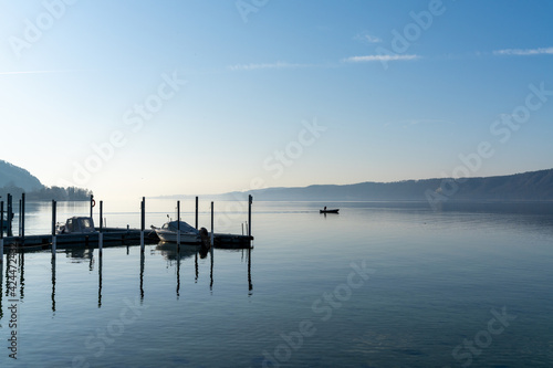 calm blue lake with moored ships and a small motorboat cruising through the water