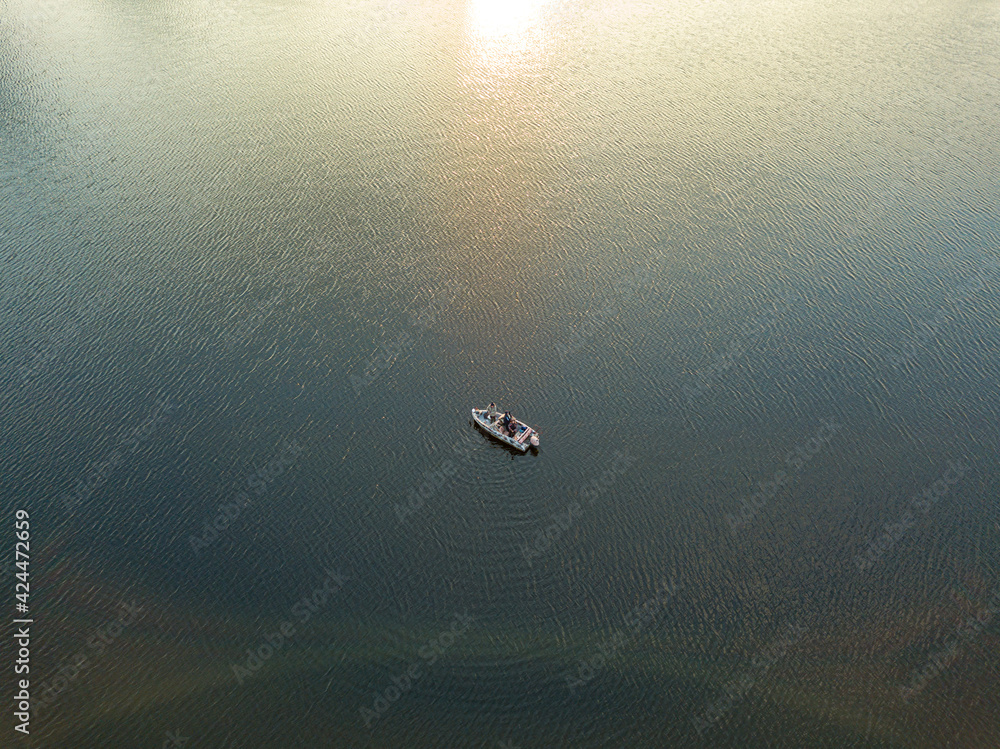 Fototapeta premium Fishing boat on the water in the rays of the sunset. Aerial drone view.
