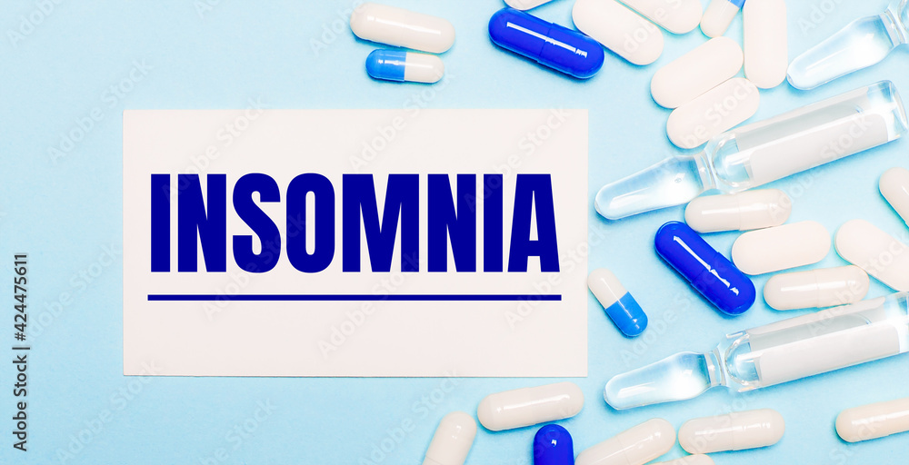 Pills, ampoules and a white card with the text INSOMNIA on a light blue background. Medical concept Pills, ampoules and a white card with the text INSOMNIA on a light blue background. Medical concept