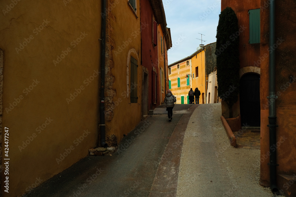 Narrow dark street of the Provencal village. The sun at the end of the street. Silhouettes of tourists. Copy space. 