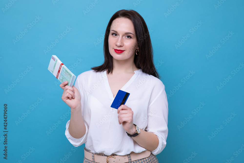 Portrait of a business woman with a wad of money and a bank card on a blue background Portrait of a business woman with a wad of money and a bank card on a blue background