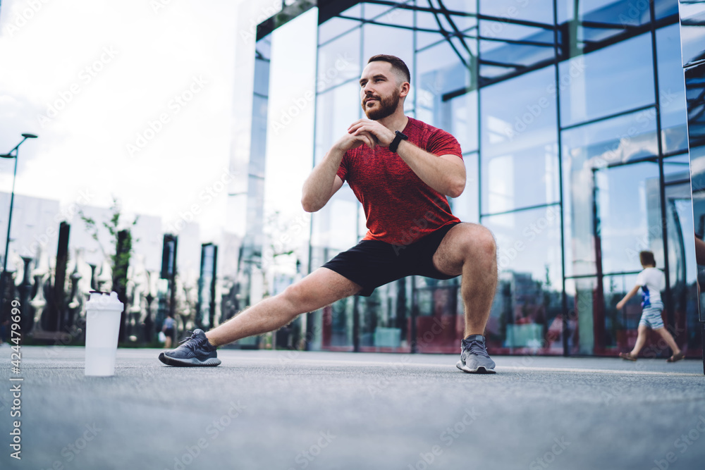 Focused sportsman stretching legs near city downtown Focused sportsman stretching legs near city downtown