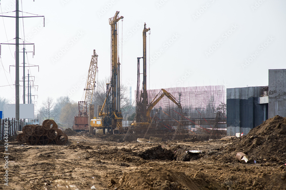 Construction site with a new concrete structure of the building in the process of construction and special equipment, an excavator, driving piles under the foundation Construction site with a new concrete structure of the building in the process of construction and special equipment, an excavator, driving piles under the foundation