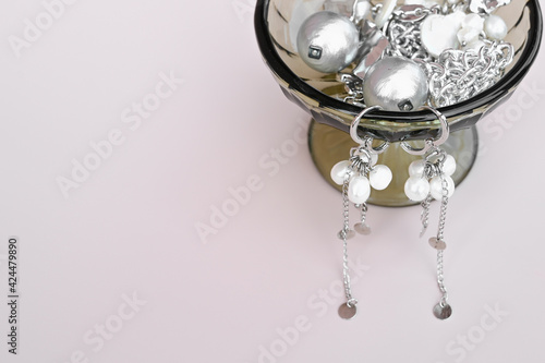 Various pieces of woman jewelry, necklace aand earrihgs, arranged against pastel pink background. 