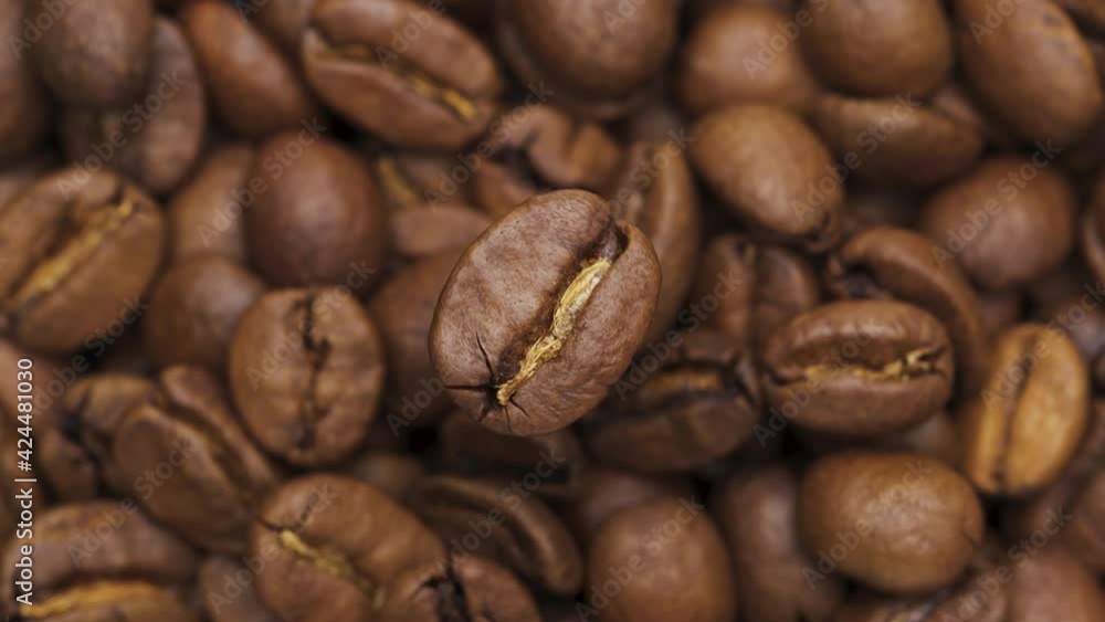 One coffee bean spinning rapidly on a dark background. Coffee beans spill out onto the table. One coffee bean spinning rapidly on a dark background. Coffee beans spill out onto the table.