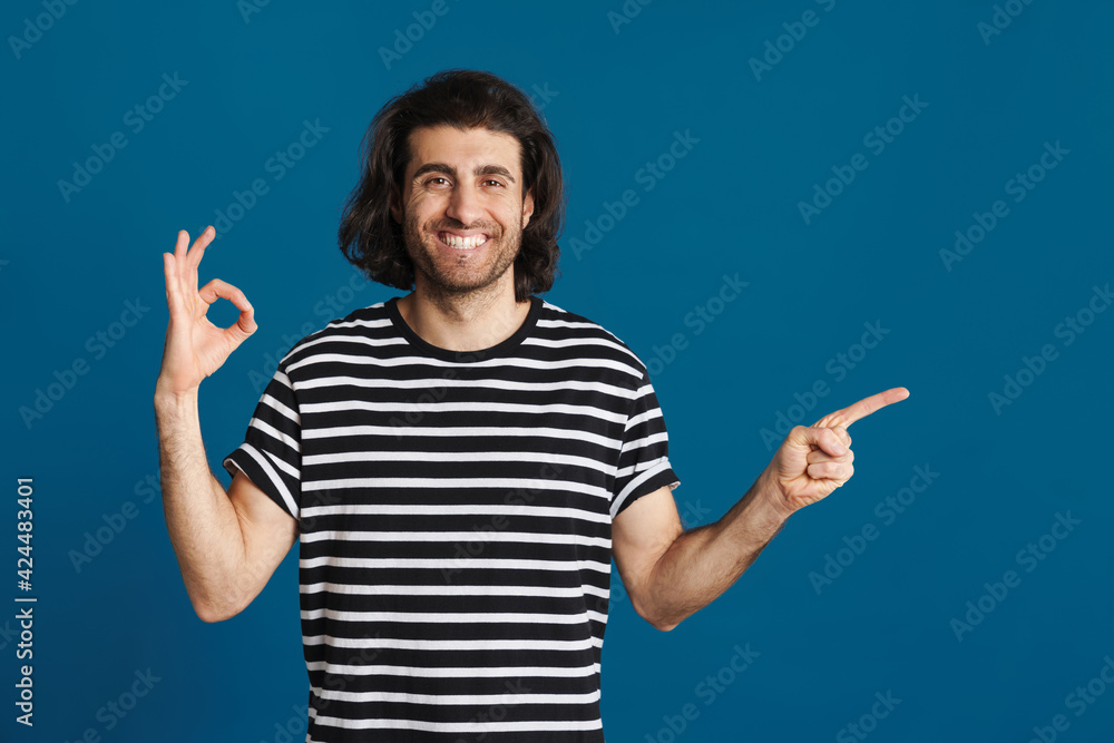 Smiling brunette man gesturing ok sign and pointing finger aside Smiling brunette man gesturing ok sign and pointing finger aside