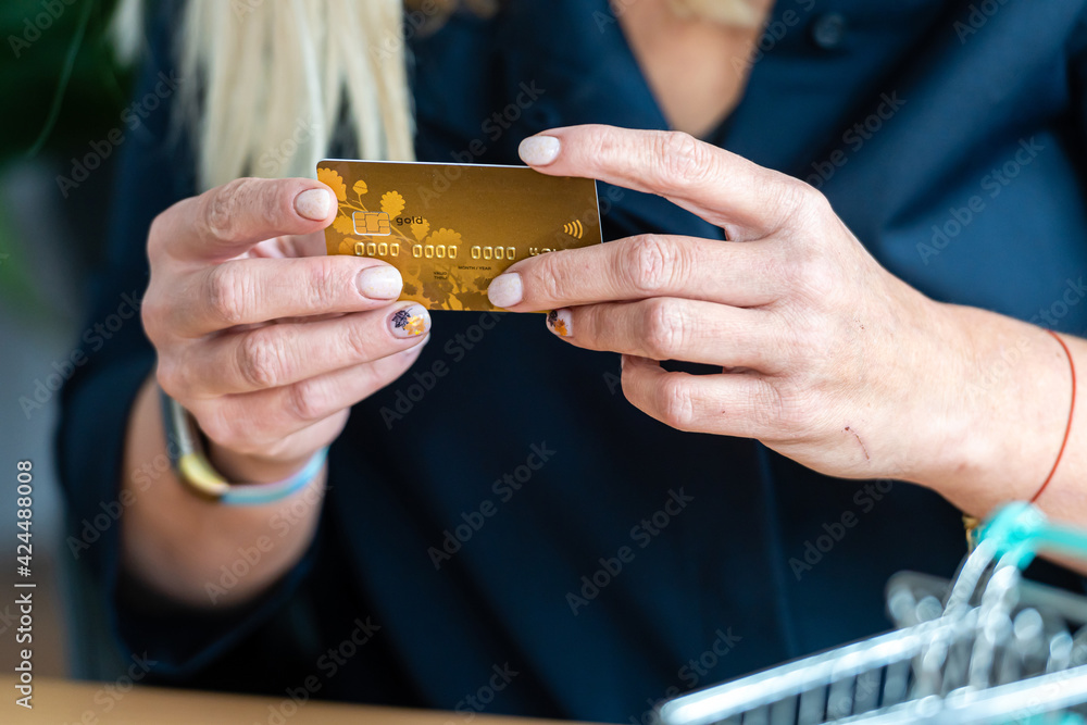 female holding credit card in hand, mini shopping cart in background, non-cash payment concept