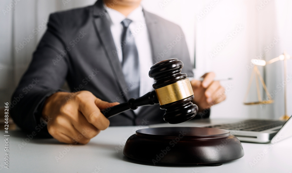 Justice and law concept.Male judge in a courtroom with the gavel, working with, computer and docking keyboard, eyeglasses, on table in morning light Justice and law concept.Male judge in a courtroom with the gavel, working with, computer and docking keyboard, eyeglasses, on table in morning light