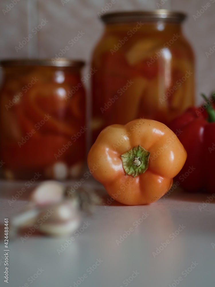 Vertical close up shot of an orange bell pepper and a garlic with jars of canned bell peppers in the backdrop. Vertical close up shot of an orange bell pepper and a garlic with jars of canned bell peppers in the backdrop.