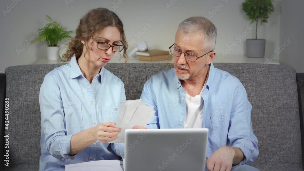 An agitated elderly couple checks unpaid debts on a laptop and gets upset. An agitated elderly couple checks unpaid debts on a laptop and gets upset.