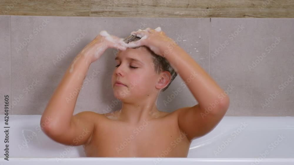 Boy washes his head with shampoo or gel while sitting in the bathroom. Child bathes at home, healthy childhood