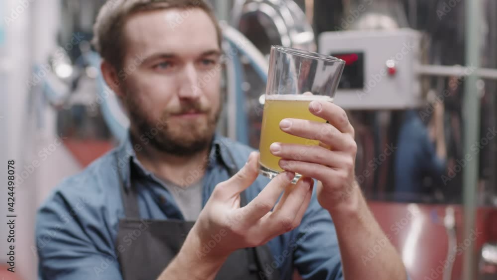 Slow-motion medium closeup of professional brewery worker looking at glass of freshly made beer doing quality check Slow-motion medium closeup of professional brewery worker looking at glass of freshly made beer doing quality check