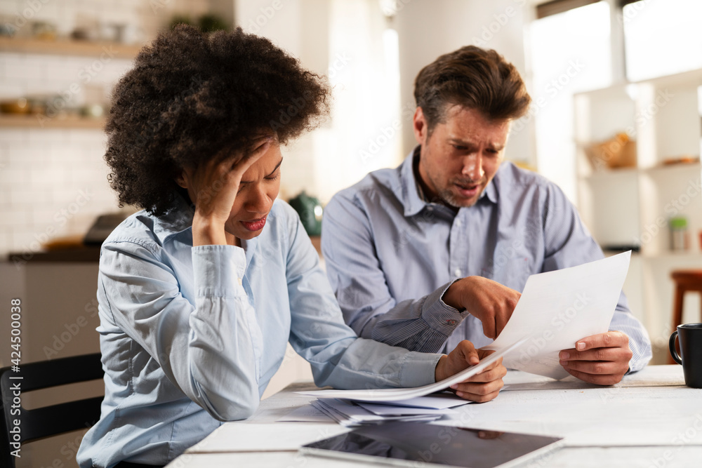 Young couple sitting in the kitchen preparing bills to pay. Stressed woman and man having financial problems. Young couple sitting in the kitchen preparing bills to pay. Stressed woman and man having financial problems.