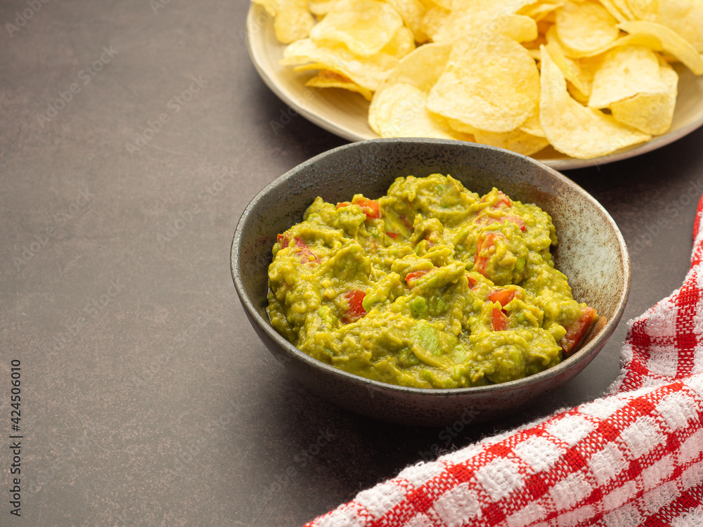 Fresh guacamole and crispy potato chips on a plate placed on dark brown background with copy space for text. Top view. Concept of traditional Mexican foods and healthy fruits Fresh guacamole and crispy potato chips on a plate placed on dark brown background with copy space for text. Top view. Concept of traditional Mexican foods and healthy fruits