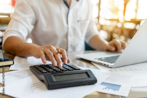 Businessman pressing on calculator for calculating cost estimating with laptop.