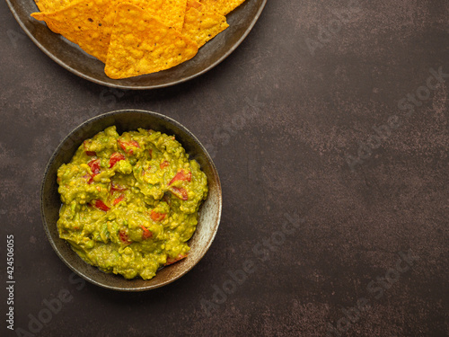 Fresh guacamole and tortilla chips on a plate placed on dark brown background with copy space for text. Top view. Concept of traditional Mexican foods and healthy fruits