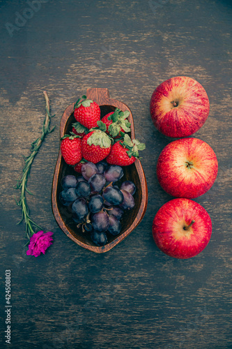 Delicious fruits on a wooden table. Strawberries, grapes and apples. Space for text. Top view.