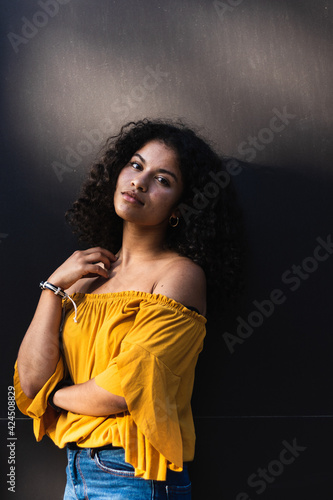 Woman with curly hair looking serious at the camera. Black wall on background