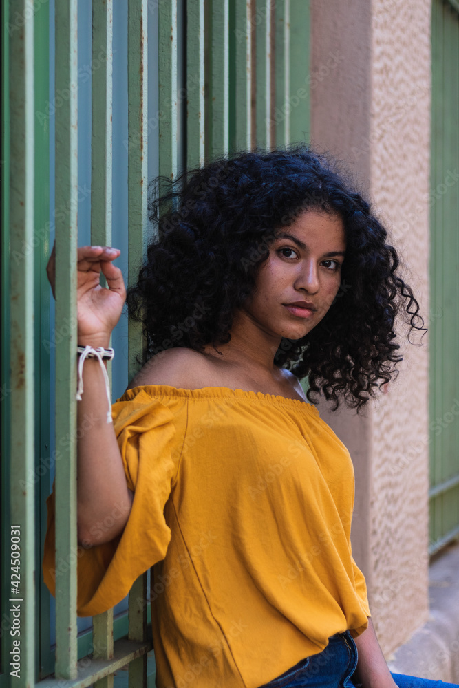 Woman with curly hair in yellow shirt looking serious at the camera Woman with curly hair in yellow shirt looking serious at the camera