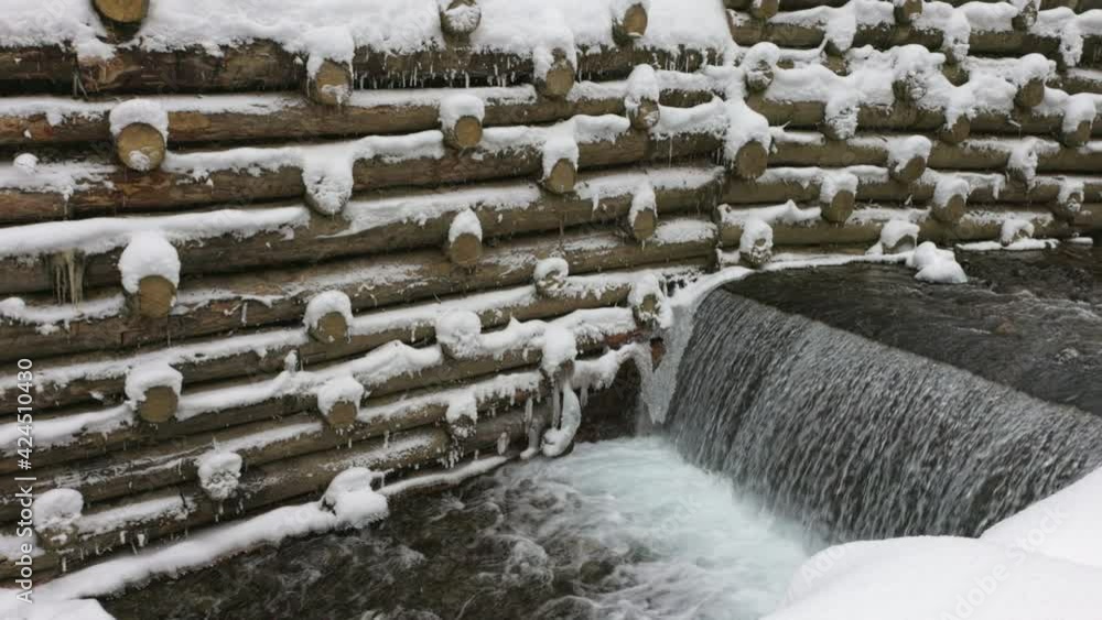 A small wall of small logs encloses a mountain stream with waterfalls in a winter forest near bare trees in the Carpathian mountains, 3X slow-motion A small wall of small logs encloses a mountain stream with waterfalls in a winter forest near bare trees in the Carpathian mountains, 3X slow-motion