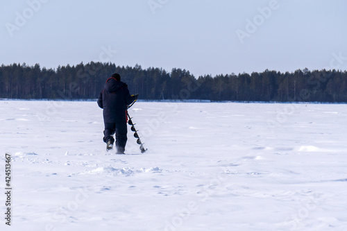fisherman on a winter lake drills the ice with a motor drill