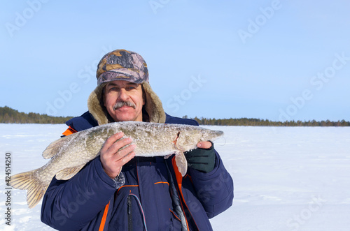 adult male fisherman with a pike catch on a winter lake. Winter fishing