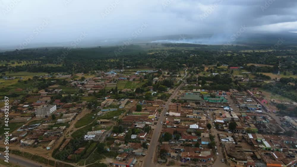 Aerial view over the Loitokitok village in the Amboseli area of Kenya, tropical forest fire background - rising, drone shot Aerial view over the Loitokitok village in the Amboseli area of Kenya, tropical forest fire background - rising, drone shot