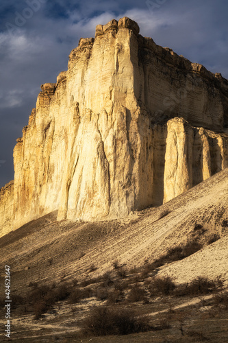 Beautiful white mountain peak lit by sun. White clouds and blue sky on background. Epic rock formation