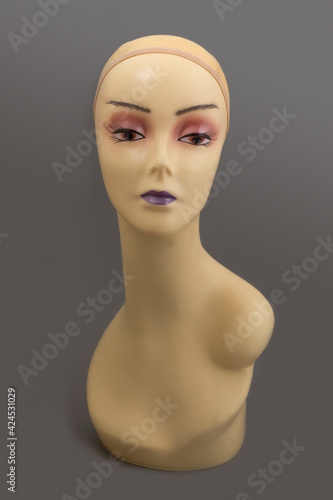 Mannequin full face of a woman's head with makeup without hair on a gray background. Fashion accessories store model for jewelry, wigs, hats, glasses, etc.