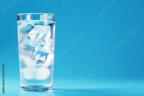 A glass with ice and clean water on a blue background.