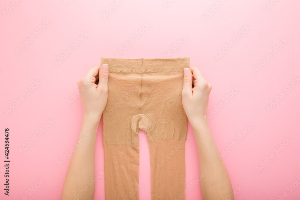 Young adult woman hands holding brown nylon pantyhose on light pink table background. Pastel color. Closeup. Point of view shot. Top down view. Young adult woman hands holding brown nylon pantyhose on light pink table background. Pastel color. Closeup. Point of view shot. Top down view.