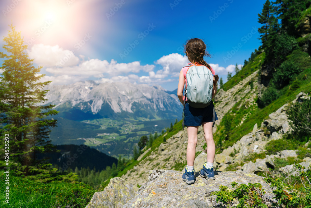 Children hiking on beautiful summer day in alps mountains Austria, resting on rock and admire amazing view to mountain peaks. Active family vacation leisure with kids. Outdoor fun and healthy activity