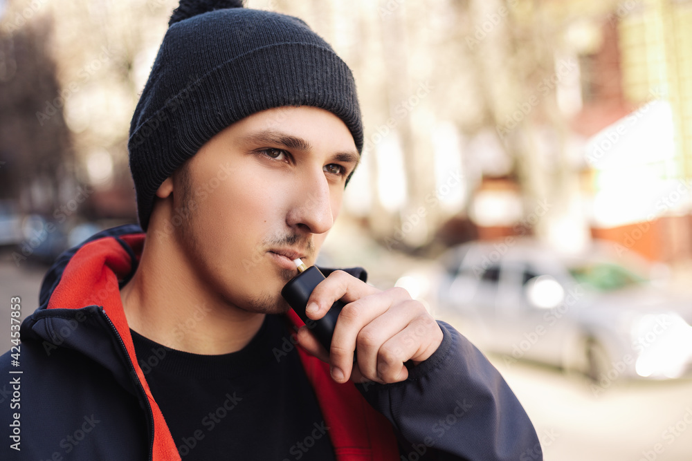 Young adult man outside and smoking tobacco device electronic cigarette heater. Smoke and steam