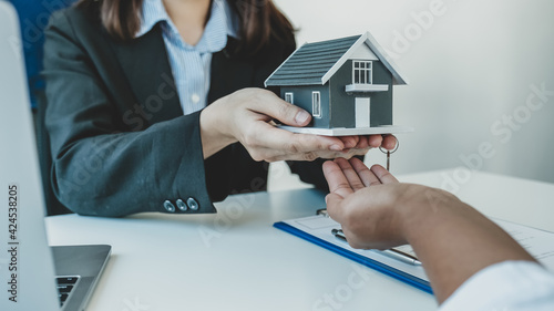 Hand a real estate agent hold the home model, and explain the business contract, rent, buy, mortgage, loan, or home insurance to the buyer woman