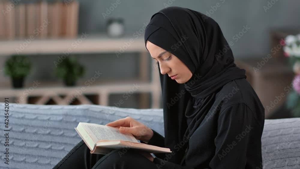 Saudi woman read holy Muslim book on comfortable sofa at cosiness home. Shot with RED camera in 4K