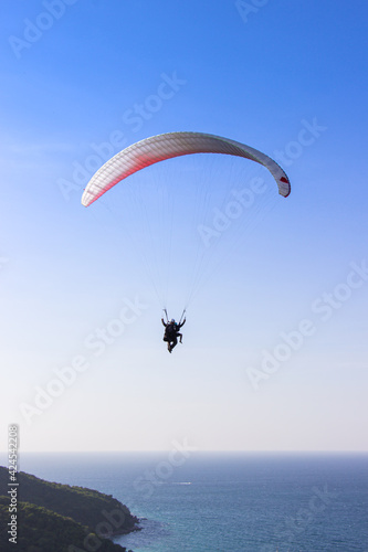 Paraglider flying over lush green mountains from view point on Koh Larn island in Pattaya, Chonburi Thailand.