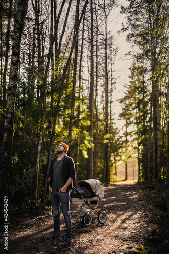 portrait of attractive nerd with glasses in the forest walks with a baby. Happy fatherhood with the wagon