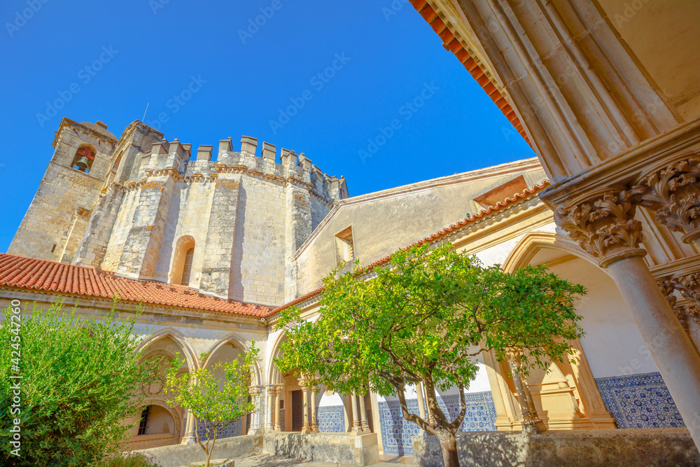 Obraz premium Tomar, Portugal - August 10, 2017: Claustro do Cemiterio near Charola of Templar Castle in Tomar on blue sky.The courtyard is in Gothic style surrounded by a porch with arcades covered with Azulejos