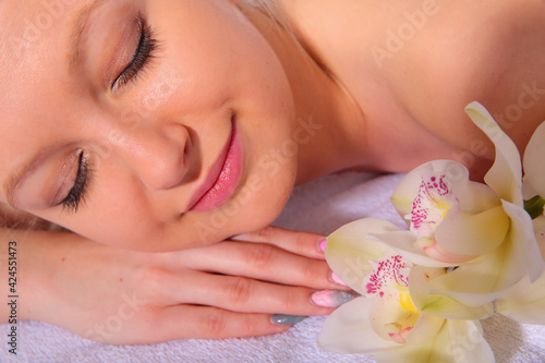 A young girl relaxes in a spa while lying on her stomach next to orchid flowers and heated stones. Close-up view