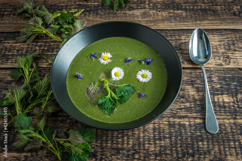 Healthy green spring nettle soup with edible flowers garnished with nettle leaves and spoon served on Green Thursday