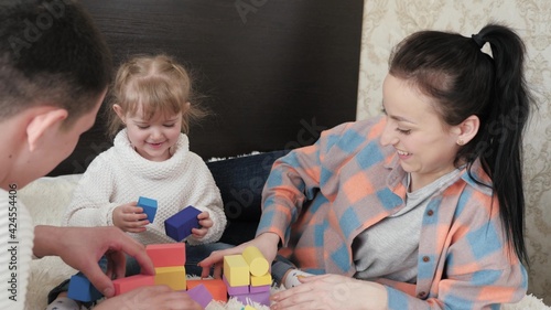 Child, father and mother are playing building family home. Happy family. Educational games for children. Dad, mom, daughter plays with cubes in nursery on bed. Teaching a child through play activities