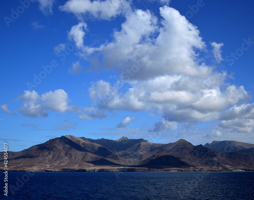 Calm sea, low clouds over the mountains and intense blue sky, coast of Jandia, Fuerteventura, Canary Islands